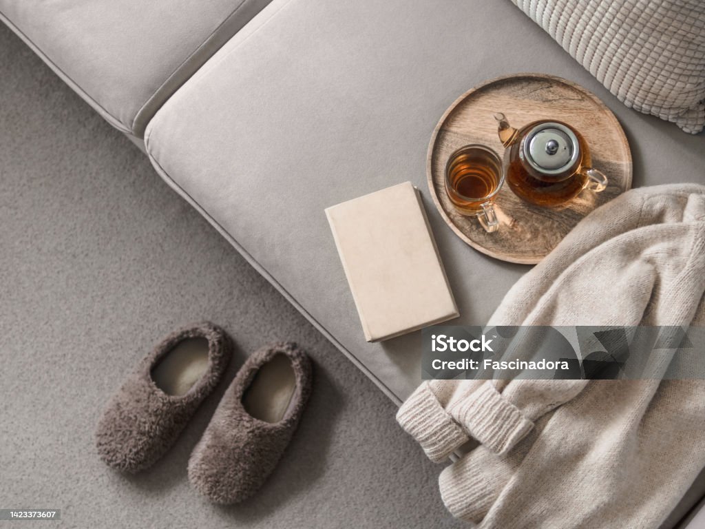 Winter cozy detail, scandi interior aesthetics Cashmere sweater, reading and serving tray on gray sofa. Warm weekend at home aesthetics. Detail of cozy scandinavian winter interior. Warm soft winter slipper on carpet at home Slipper Stock Photo