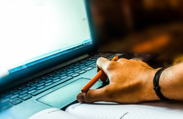 istock Close-Up Of Men Hand Using Laptop With Notepad and Pen on Table 1423373716