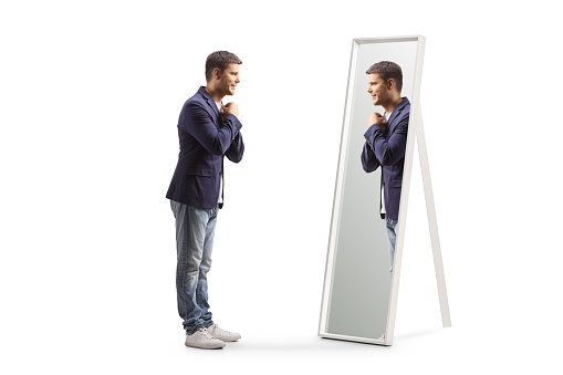 Full length profile shot of a young man getting ready and looking at a mirror isolated on white background