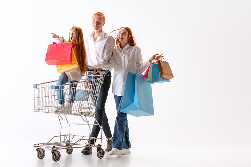 Wow. Happy and excited family, young readhaired people walking together after shopping with purchases in hands isolated on white bakground. Concept of black Friday, holidays, fashion, dreams