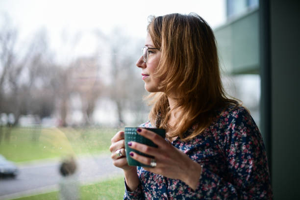istock Woman drinking coffee and looking out the window in room 1423374280