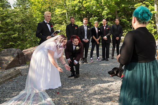 Lesbian brides at LGBTQ+ wedding ceremony outdoors in summer. Guest is bringing service dog. This is part of a series about a lesbian couple getting married. Horizontal outdoors full length shot with copy space.
