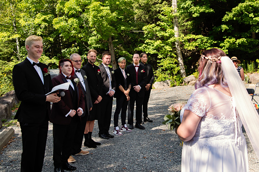 Lesbian brides at LGBTQ+ wedding ceremony outdoors in summer. Grooms are standing beside red hair bride. This is part of a series about a lesbian couple getting married. Horizontal outdoors waist up shot with copy space.