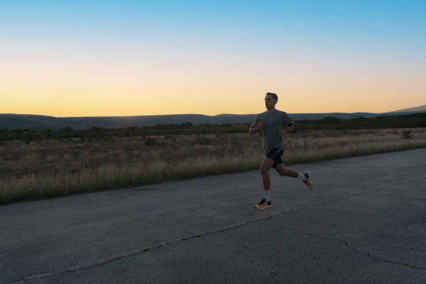 istock Attractive fit man running fast along countryside road at sunset light, doing jogging workout outdoors 1423377413