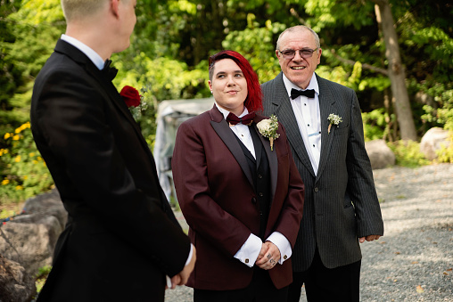 Father walking daughter bride down the aisle for LGBTQ+ wedding. This is part of a series about a lesbian couple getting married. Horizontal outdoors waist up shot with copy space.