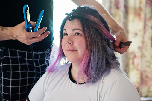 Body positive woman having her hair done for LGBTQ+ wedding. She is one of the brides, and this is part of a series about a lesbian couple getting married. Horizontal indoors waist up shot with copy space.