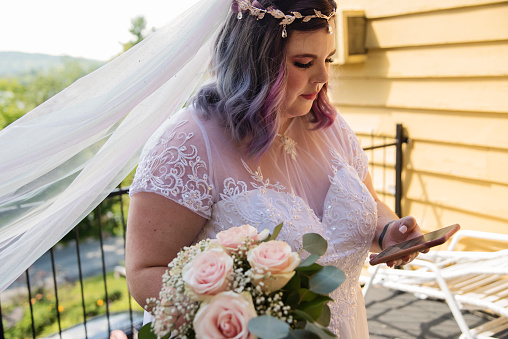 Portrait of beautiful body positive future bride with mobile phone before LGBTQ+ wedding. This is part of a series about a lesbian couple getting married. Horizontal outdoors full length shot with copy space.