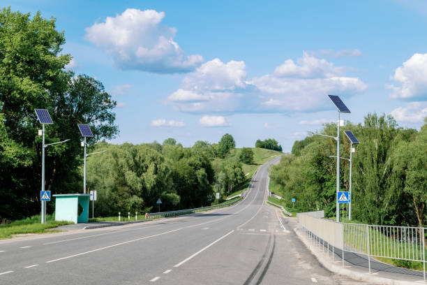 poste de luz com sistema de painéis solares na estrada com céu azul e árvores. iluminação pública autônoma usando painéis solares. lâmpada de rua, em baterias do sol. sistemas alternativos de energia renovável nas ruas. - choice street road beginnings - fotografias e filmes do acervo