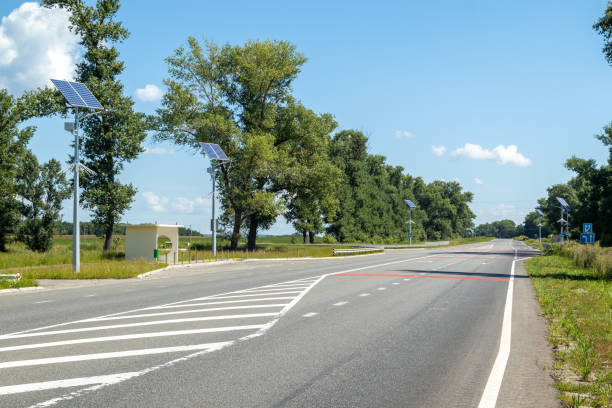 poste de luz com sistema de painéis solares na estrada com céu azul e árvores. iluminação pública autônoma usando painéis solares. lâmpada de rua, em baterias do sol. sistemas alternativos de energia renovável nas ruas. - choice street road beginnings - fotografias e filmes do acervo