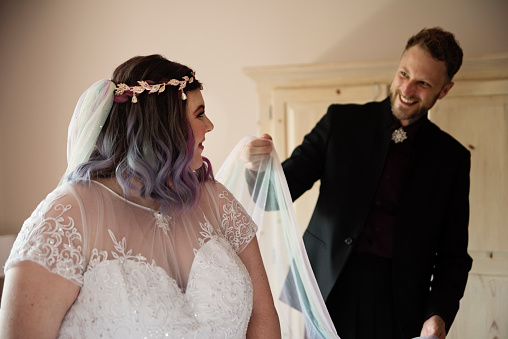 Body positive future bride getting ready with the help of a dear friend before LGBTQ+ wedding. This is part of a series about a lesbian couple getting married. Horizontal indoors waist up shot with copy space.