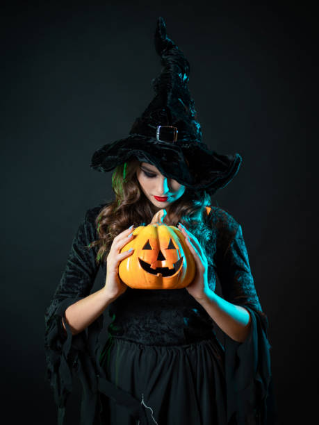 istock beautiful witch in a pointed hat Holding a pumpkin with a laughing face, 1423383099