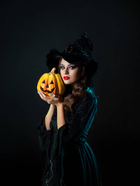 istock beautiful witch in a pointed hat Holding a pumpkin with a laughing face, 1423383109