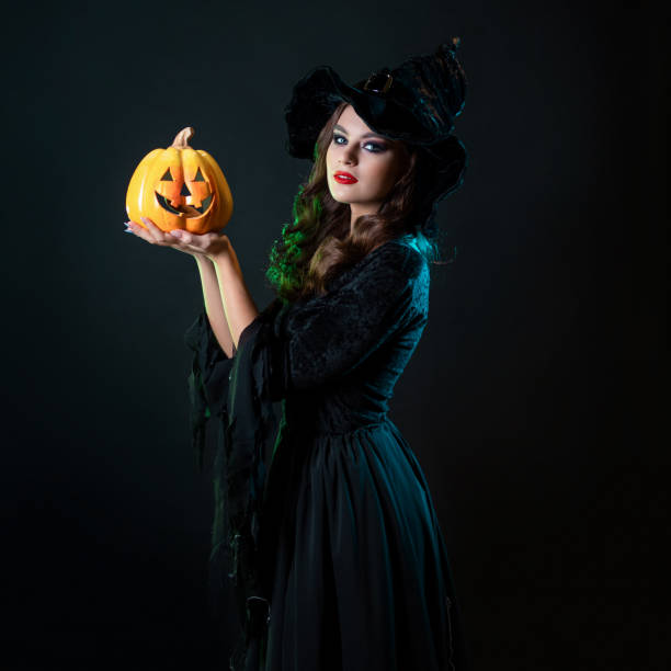 istock beautiful witch in a pointed hat Holding a pumpkin with a laughing face, 1423383164