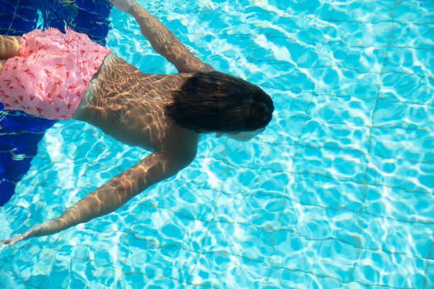 Portrait of smiling little boy enjoying underwater swim in the pool. The boy is gliding by the camera during swimming lesson. Sunny summer day.
