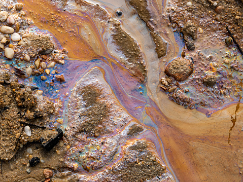 Oil spill pollution in the water and on the sand. Fossil fuel in the environment. Spectral colors of light are visible. The nature is contaminated by industrial waste.