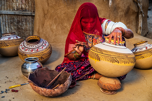 Indian woman painting water pots in her workshop, desert village in Rajasthan, India
