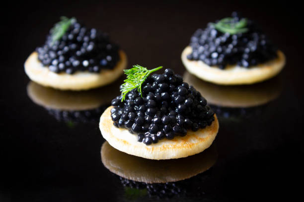 Caviar Blinis Three black caviar blinis with fresh dill, on a black background. caviar stock pictures, royalty-free photos & images