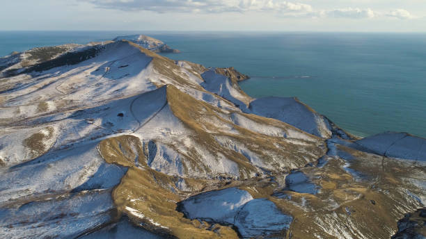 vista aerea di rocce innevate, mare blu, su sfondo cielo nuvoloso. sparo. colline innevate in islanda vicino al mare in una giornata invernale. - rear view winter blizzard nordic countries foto e immagini stock