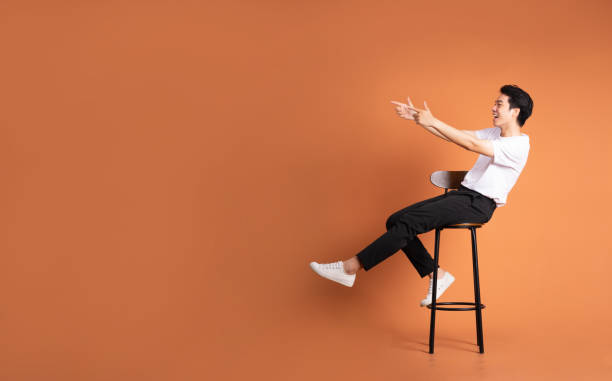 istock image of asian man sitting on a stool, isolated on orange background 1423387383