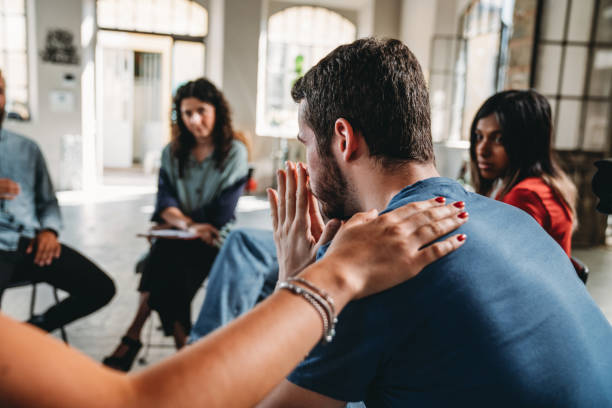 People are comforting a man during a group therapy session stock photo