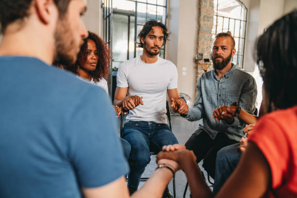 istock People are sitting in circle holding hands together during a group therapy session 1423390140