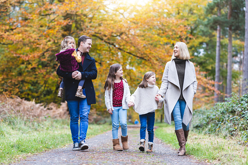 Beautiful authentic family of five people mother father daughters enjoying walk in the wood in autumn with warm fall colours - Lifestyle and family concepts