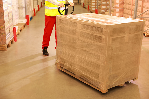 Worker moving wooden pallets wrapped in stretch indoors, closeup