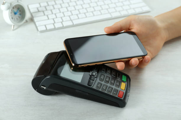 istock Woman with credit card using modern payment terminal at white table, closeup 1423392106