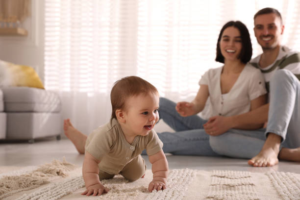 かわいい赤ちゃんが家で床に這うのを見ている幸せな両親 - mother baby child playing ストックフォトと画像