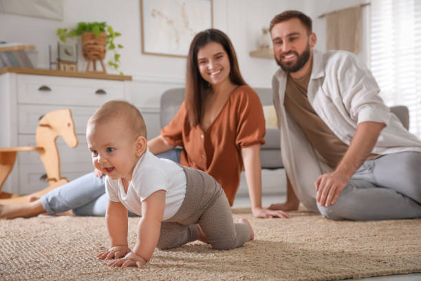 赤ちゃんが家で床に這うのを見ている幸せな両親 - mother baby child playing ストックフォトと画像