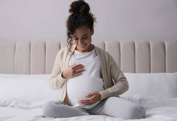 grávida jovem afro-americana sentada na cama em casa - anticipation built structure indoors image technique - fotografias e filmes do acervo