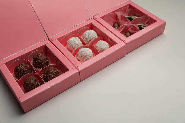 Delicious candies in pink boxes on light grey background. Production line