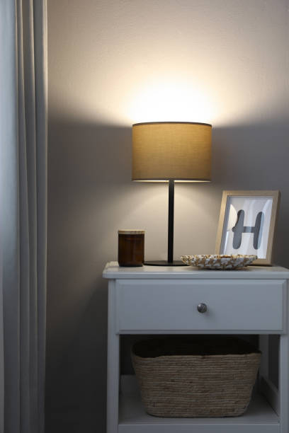istock Stylish lamp and decor on white nightstand in room 1423393216