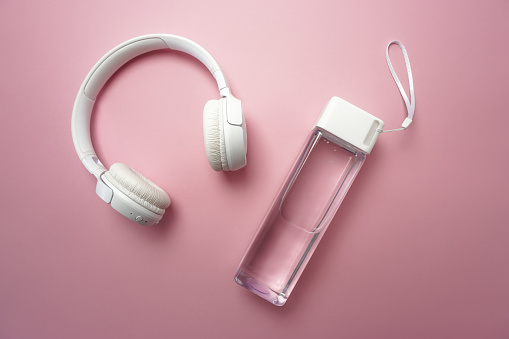 On a pink background there is a bottle of clean water and white headphones