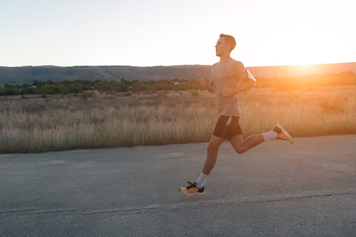 Attractive fit man running fast along countryside road at sunset light, doing jogging workout outdoors. High quality photo