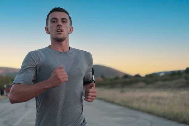 istock Attractive fit man running fast along countryside road at sunset light, doing jogging workout outdoors 1423397203