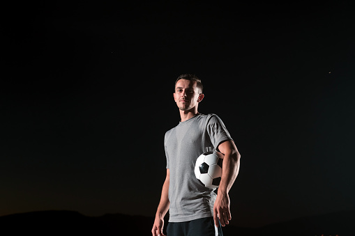 portrait of a young handsome talented soccer player man on a street playing with a football ball. High quality photo