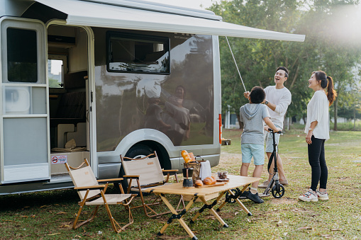 Image of an Asian Chinese family setting up awning and preparing for a caravan picnic vacation at public park