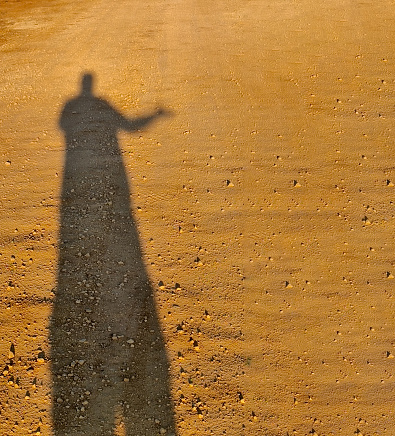 Long shadows of a person on a ground of dirt and stones while walking with selective focus.