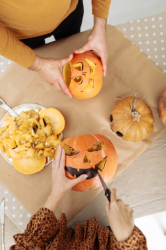 Young couple man and woman on kitchen at home making jack-o'-lantern preparing for halloween, cutting pumpkin. Cutting out faces from a fresh pumpkin. Preparing for the Halloween party celebration