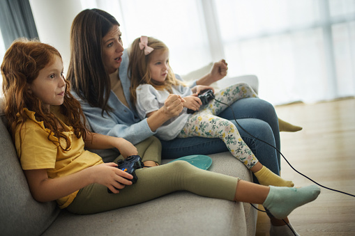 Closeup of two sisters playing video games with their mother.