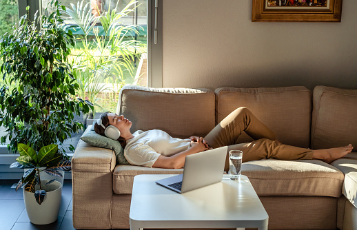 Young woman having online hypnotherapy regression session with psychotherapist lying on sofa at home. Digital service