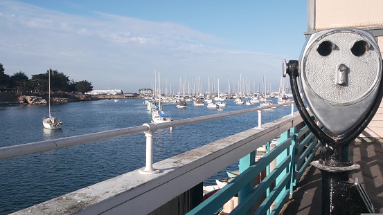 Yachts in harbor or bay, Monterey marina, Old Fishermans Wharf, quay or pier, California coast USA. Stationary binoculars, tower viewer or telescope by ocean sea water. Beachfront waterfront boardwalk
