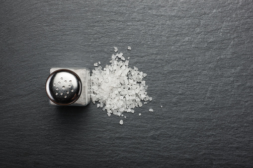salt shaker with white salt on black stone background, top view