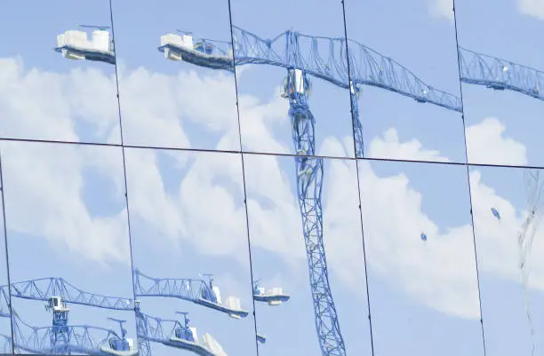 Blue construction cranes and sky reflected in panes of shiny glass