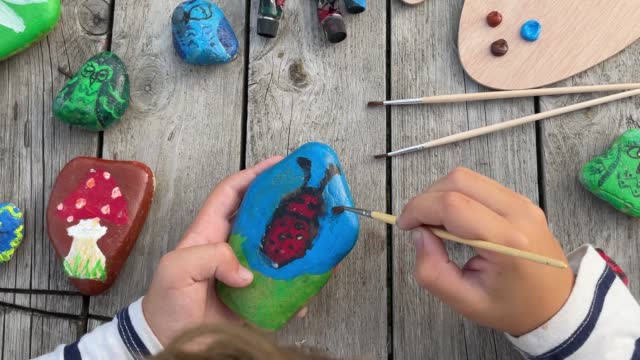 footage of a child's hands drawing a fungus on a stone with acrylic paints. Home hobbies are authentic.