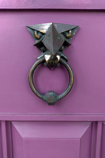 Antique metal eagle door knocker, door element with metal handle. A manual door knocker in the form of an eagle on a purple wooden door. A very old door handle