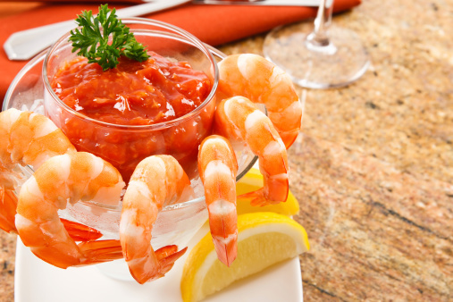 Cooked shrimp with cocktail sauce against a granite tabletop.  Shellfish like shrimp are a delicious appetizer but also pose a health risk to anyone with a food allergy to shellfish.
