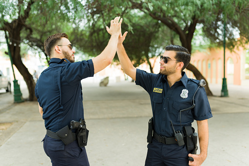 Successful male police partners doing a high five and celebrating after making an arrest of a street criminal