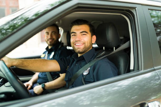 Cheerful police officer on duty driving the patrol car Happy cop agent smiling while on patrol in the police car on the street and enjoying law enforcement police force smiling officer stock pictures, royalty-free photos & images